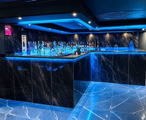 Modern bar interior with black marble walls, blue neon lighting, illuminated shelves of bottles, and polished marble floor