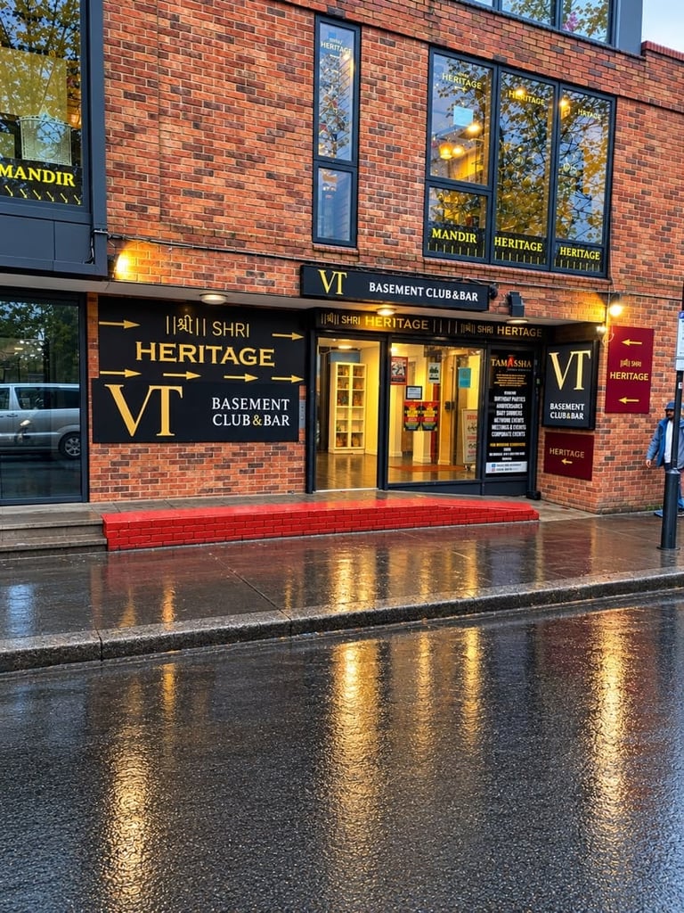 Storefront of VT Heritage basement club and bar in a red brick building with gold lettering and illuminated signage, wet pavement in foreground