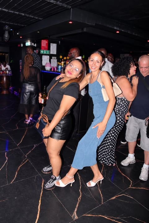 Group of people enjoying drinks and dancing at a nightclub with black marble floor and neon signs